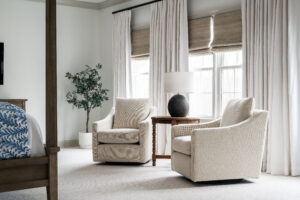 bedroom seating area with two cream swivel chairs, custom linen curtains, natural woven shades, plant in corner.
