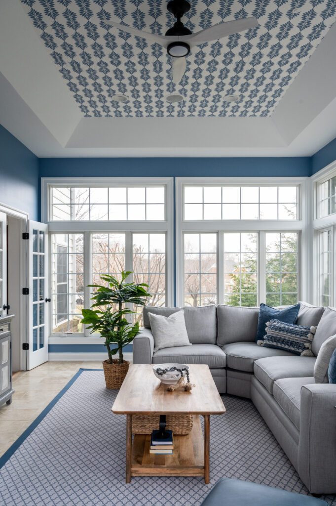 blue and white sunroom with grey sectional and wallpapered ceiling