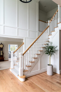 Foyer with custom millwork and stairs, plant and black wagon wheel chandelier