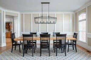 Custom living room. Black cage chandelier above a custom live edge table surrounded by black dining chairs. The walls are adorned with custom shaker millwork. The floor is covered with a custom sized blue patterned rug.