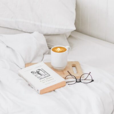 Bed with white linens and a book, coffee, and glasses