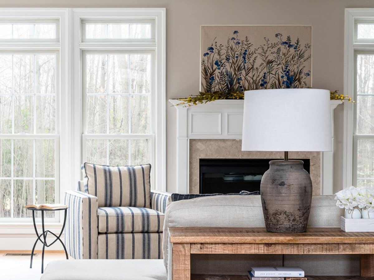 Rustic table lamp sitting on wooden console with blue striped chair in the background.