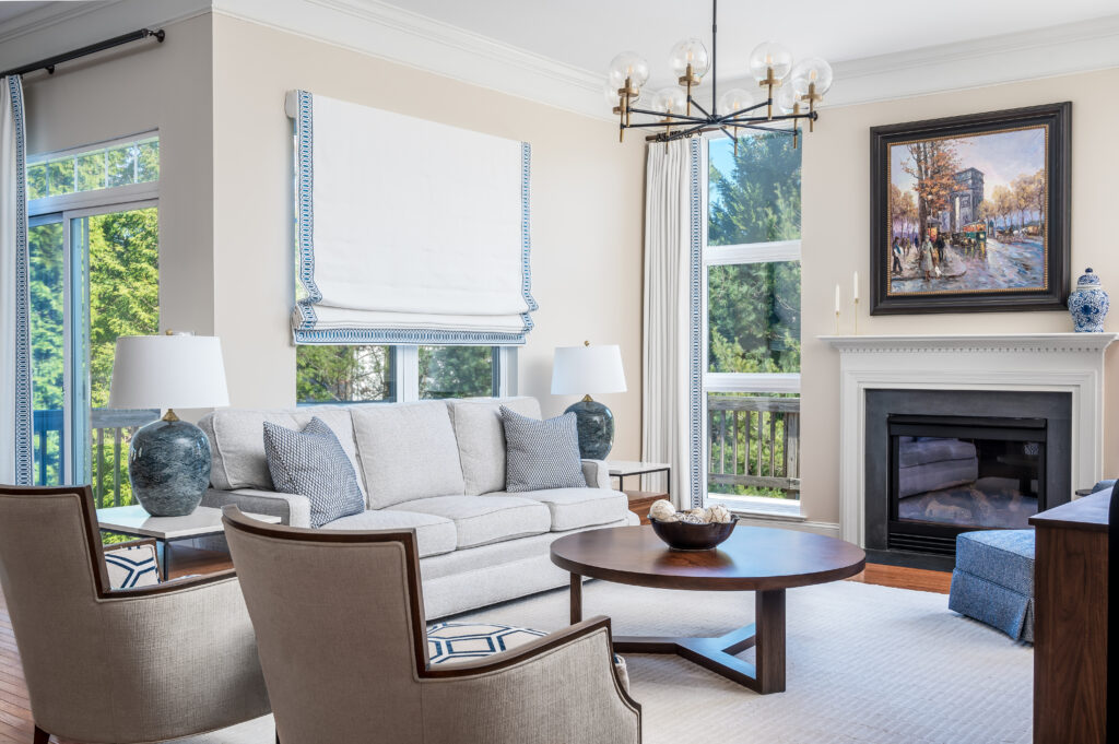 Custom living room design featuring elegant window treatments, a cozy fireplace, a comfortable sofa, and two custom chairs with dual fabric. A modern chandelier hangs from the ceiling, providing a stylish and functional source of lighting.