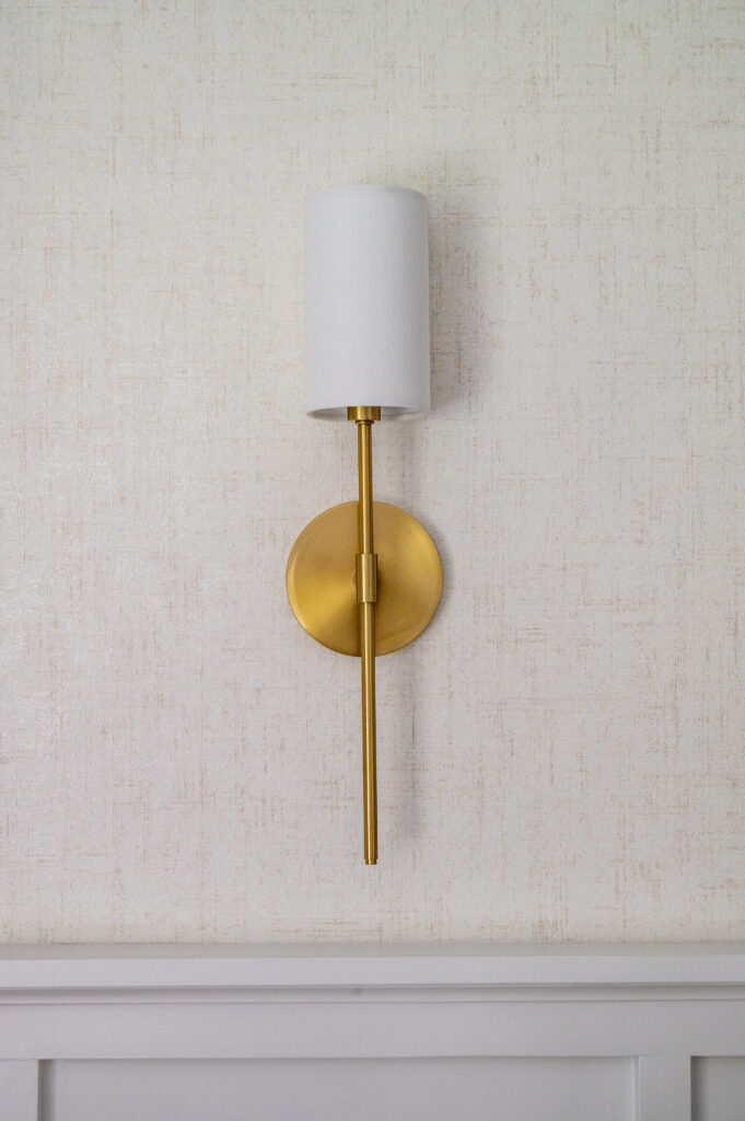Golden wall sconce with linen shade. Grasscloth wallpaper above molding