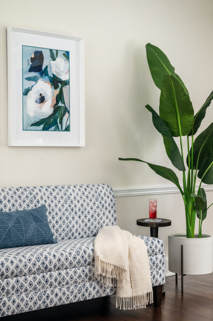 Custom upholstered bench with floral artwork, large plant, and drink table