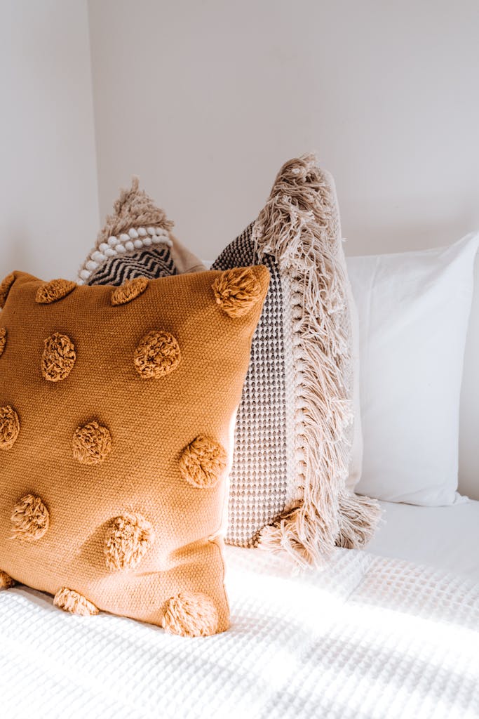 Comfortable colorful pillows placed on soft bed in light apartment illuminated by sunlight