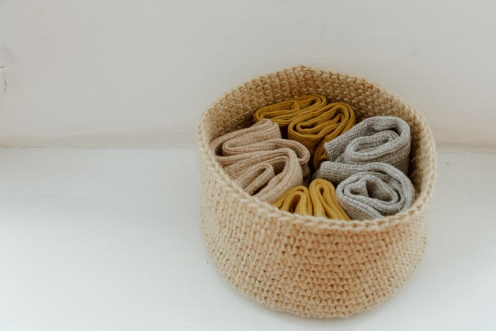 A collection of rolled knitted socks in a woven basket, showcasing organization.