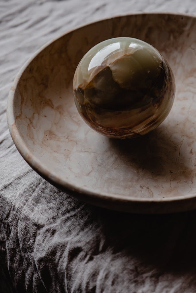 A detailed close-up of a polished stone sphere placed in a rustic ceramic bowl on a textured cloth.