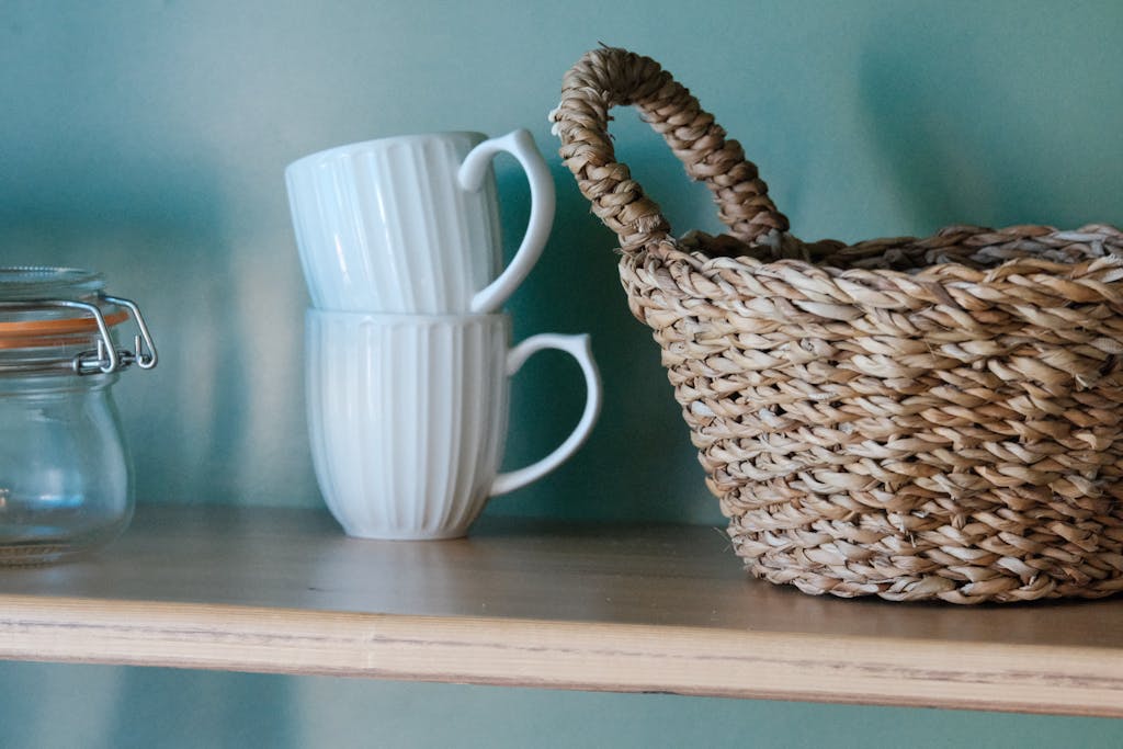 A wicker basket and stacked mugs on a wooden shelf create a rustic kitchen vibe.