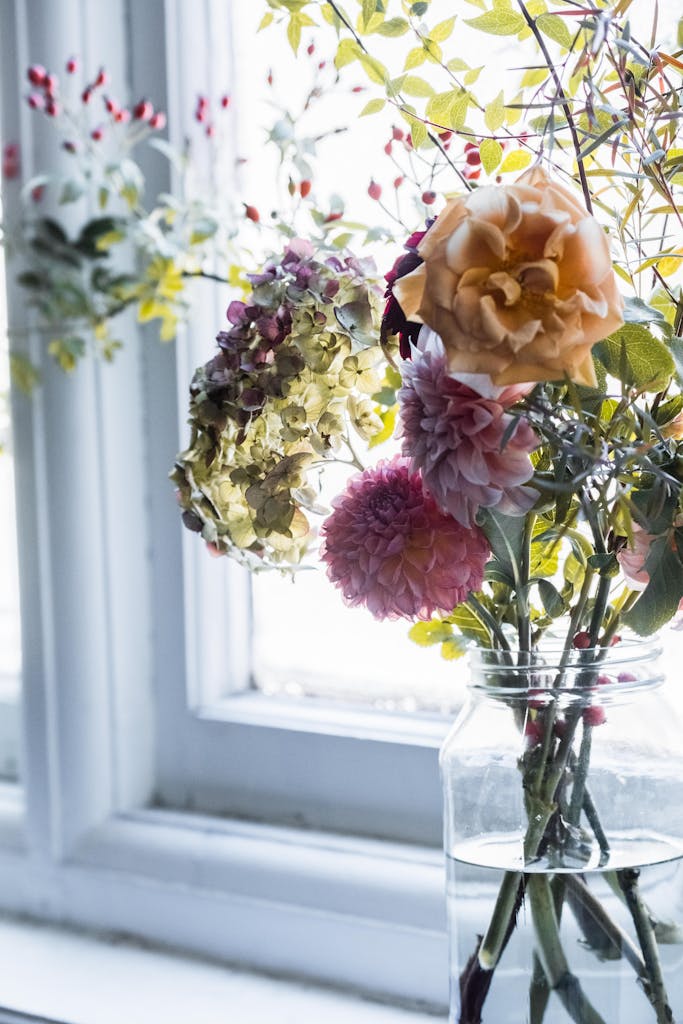 Charming floral arrangement in vase on windowsill, bathed in light.