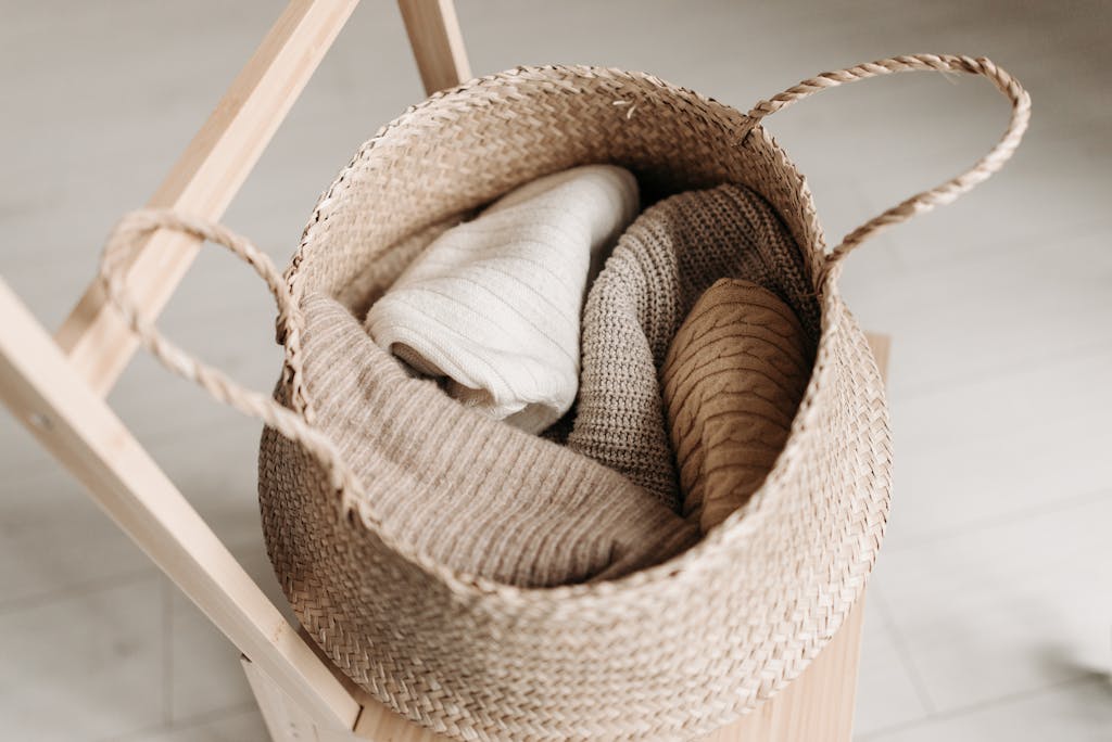 Close-up of folded knitted garments in a woven basket on a wooden chair, exuding warmth and comfort.