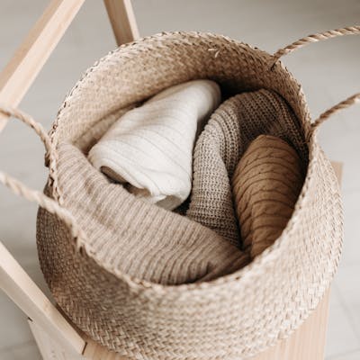 Close-up of folded knitted garments in a woven basket on a wooden chair, exuding warmth and comfort.