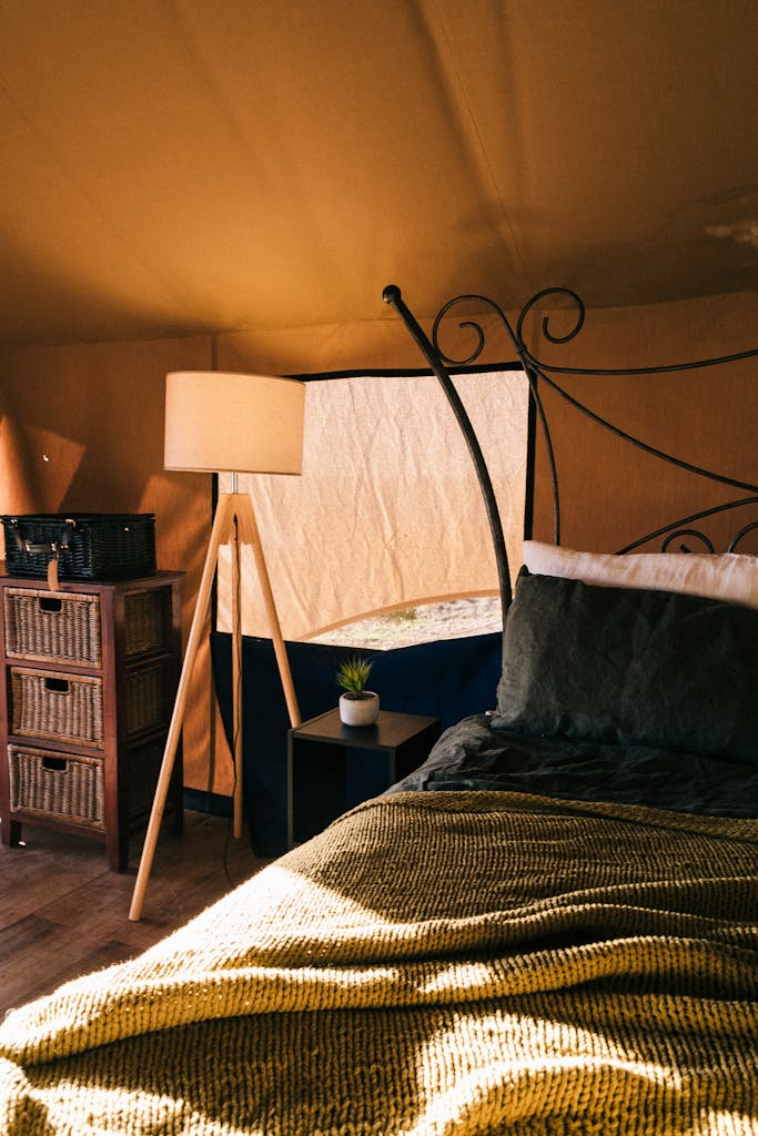 Comfortable bed with bedside table and lamp under tent roof with covered window