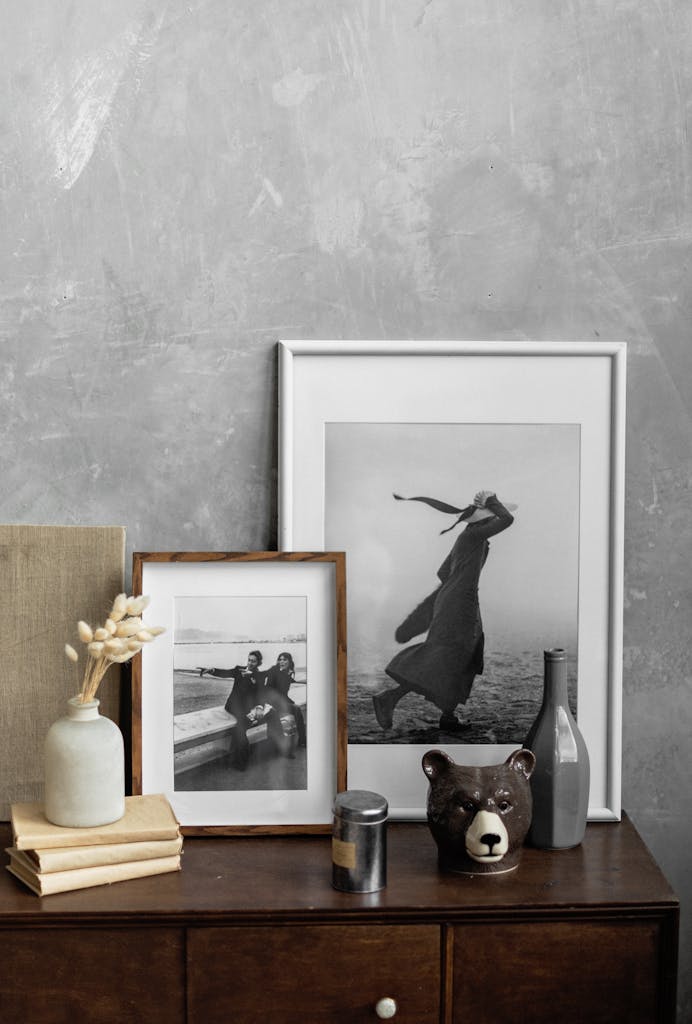 Framed black and white photos and decorative elements arranged on wooden cabinet near vase with dry reeds placed on stack of books