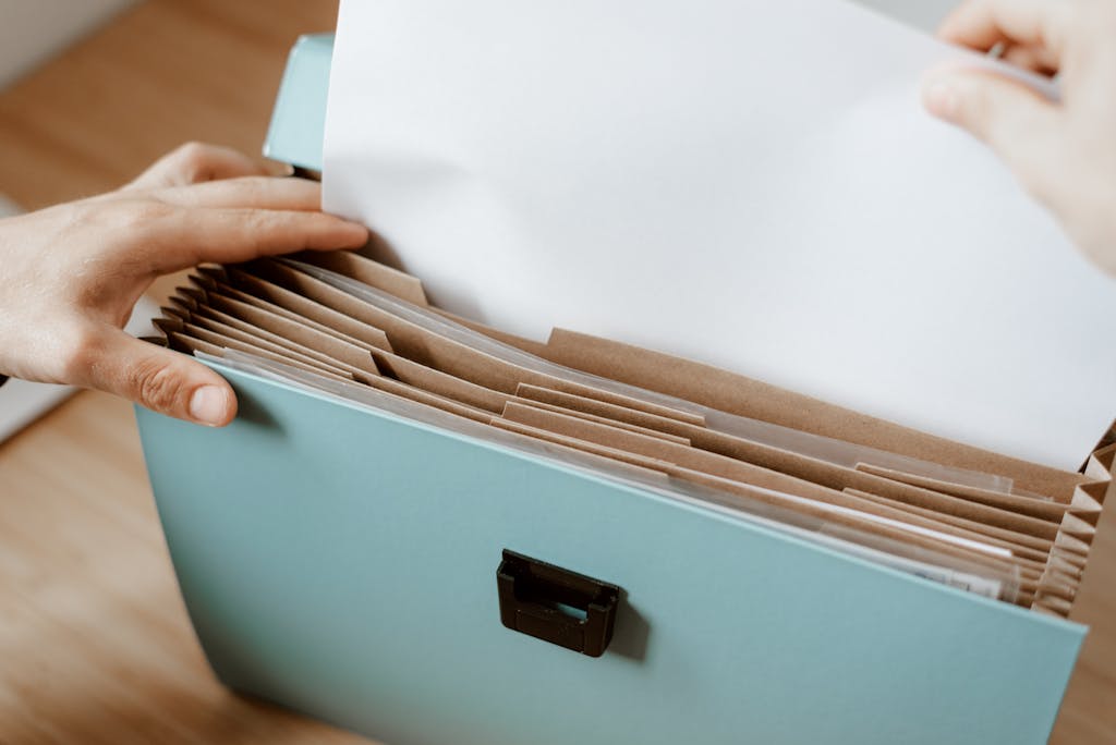 Hands organizing papers in a blue office folder with brown dividers, showing workplace efficiency.