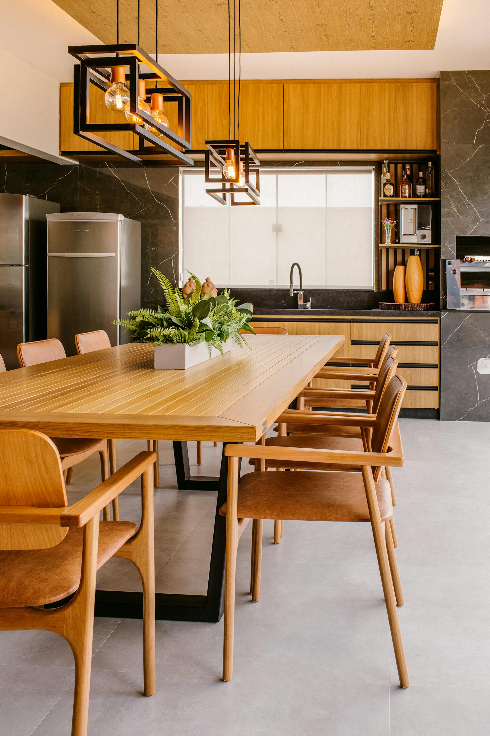 Stylish modern kitchen featuring wooden dining table with chairs, stainless steel fridge, and indoor plants.