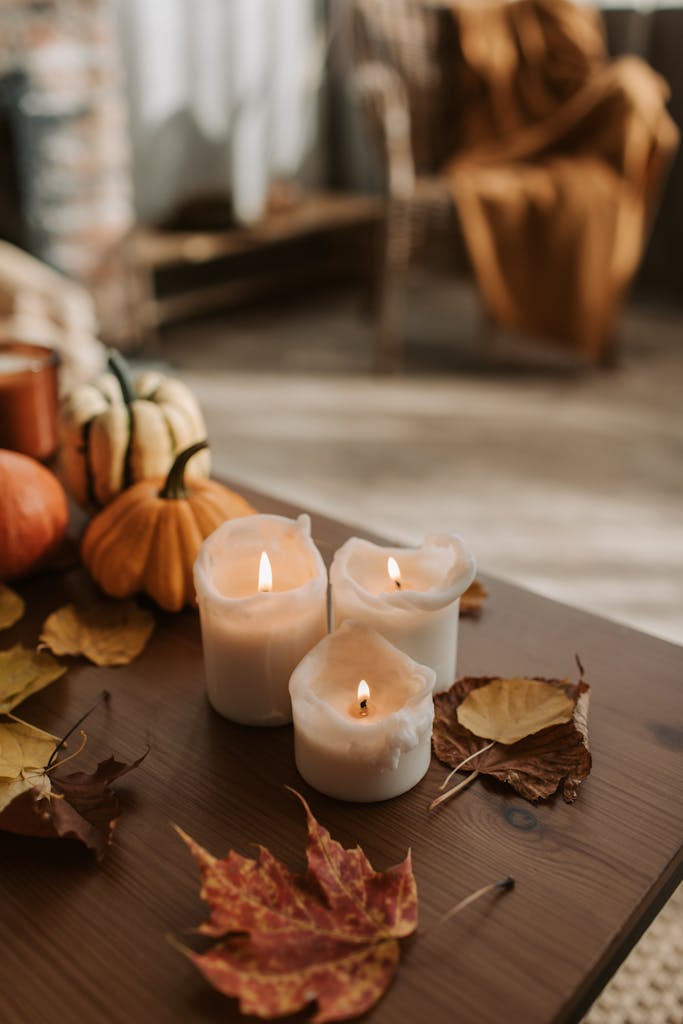 Warm autumn atmosphere with candles, pumpkins, and leaves on a rustic table.