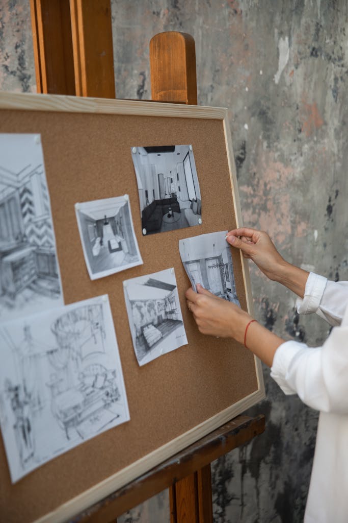 An interior designer setting up sketches on a corkboard in a studio setting.