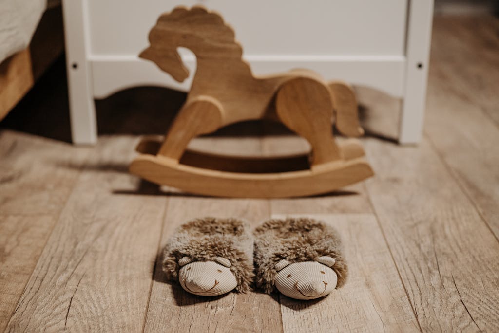 Warm, fluffy slippers on wooden floor in nursery beside a wooden rocking horse.